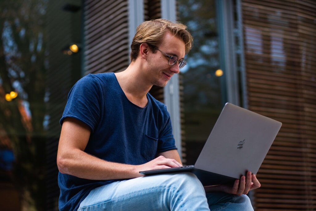 A man sitting outside smiling at his laptop